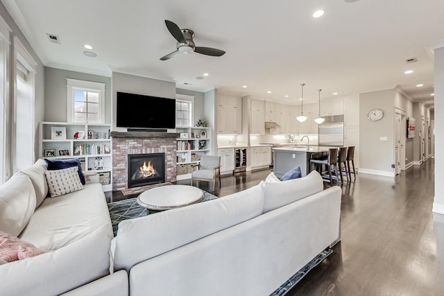 living room featuring dark hardwood / wood-style floors, a brick fireplace, wine cooler, crown molding, and ceiling fan