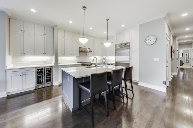 kitchen with decorative light fixtures, an island with sink, beverage cooler, built in fridge, and sink