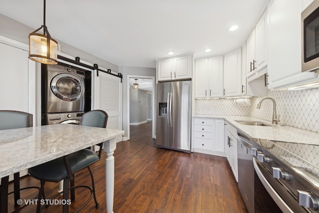 kitchen with pendant lighting, stacked washing maching and dryer, stainless steel appliances, white cabinets, and a barn door