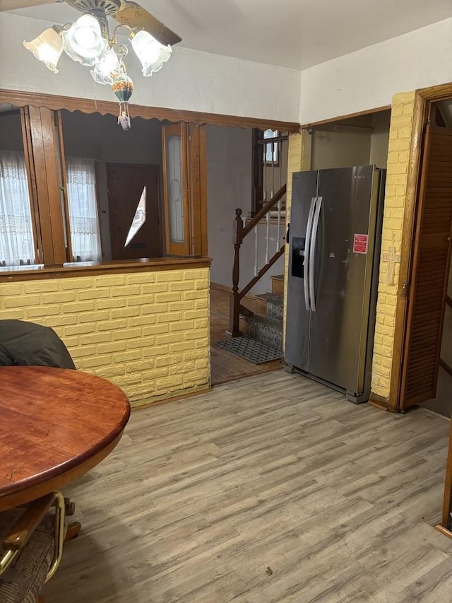 interior space featuring stainless steel fridge with ice dispenser, brick wall, and light wood-type flooring