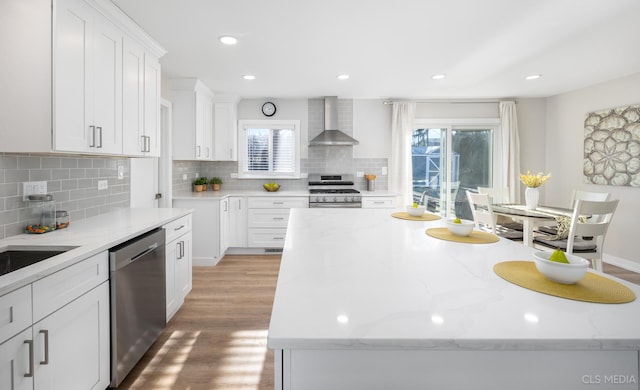 kitchen featuring white cabinetry, a center island, wall chimney exhaust hood, light stone counters, and appliances with stainless steel finishes