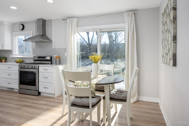 kitchen with light wood-type flooring, backsplash, wall chimney exhaust hood, stainless steel stove, and white cabinetry