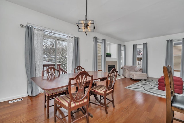 dining room featuring a tiled fireplace, hardwood / wood-style floors, and an inviting chandelier