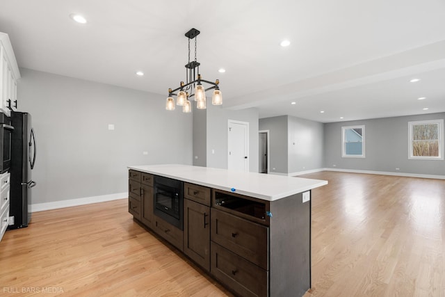 kitchen with white cabinets, hanging light fixtures, a kitchen island, black microwave, and stainless steel refrigerator