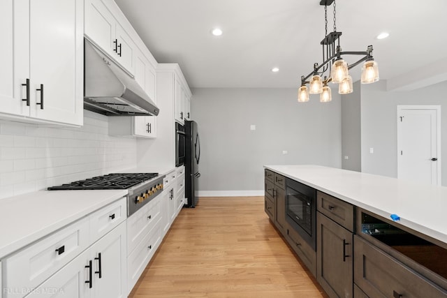 kitchen with backsplash, light wood-type flooring, appliances with stainless steel finishes, decorative light fixtures, and white cabinetry