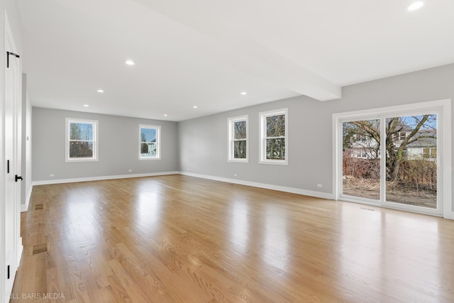 unfurnished living room featuring beamed ceiling, light wood-type flooring, and a wealth of natural light