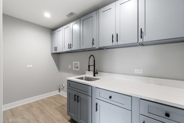 clothes washing area featuring cabinets, washer hookup, sink, light hardwood / wood-style floors, and hookup for a gas dryer