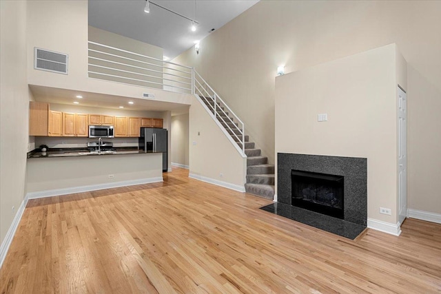 unfurnished living room with a towering ceiling, track lighting, and light hardwood / wood-style flooring