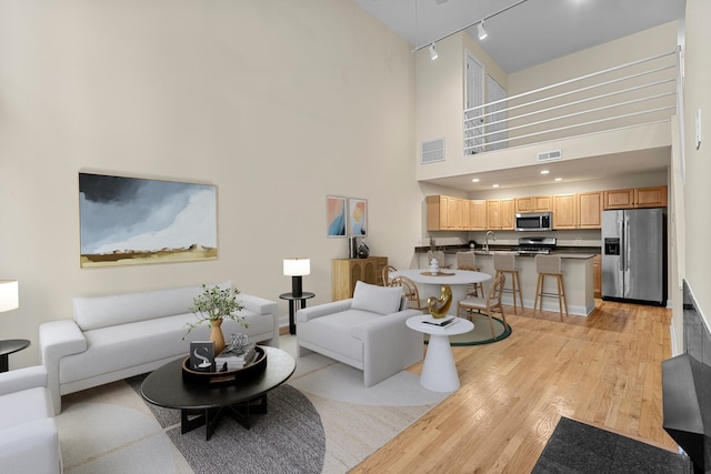 living room featuring a high ceiling, rail lighting, sink, and light wood-type flooring