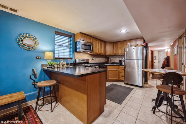 kitchen featuring sink, appliances with stainless steel finishes, tasteful backsplash, light tile patterned flooring, and kitchen peninsula