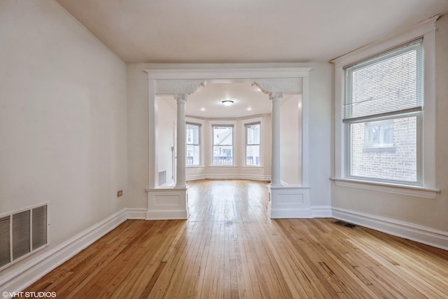 unfurnished living room featuring ornate columns and light hardwood / wood-style floors