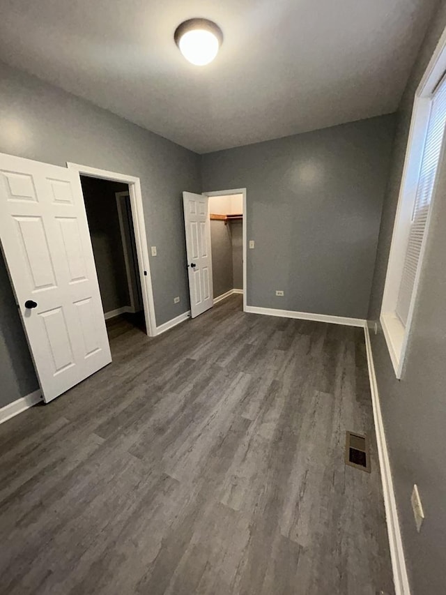 unfurnished bedroom with a spacious closet, a closet, and dark wood-type flooring