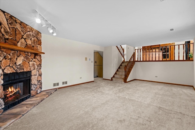 unfurnished living room featuring light colored carpet, track lighting, and a stone fireplace