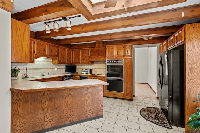 kitchen with a skylight, decorative backsplash, black fridge, kitchen peninsula, and tile countertops