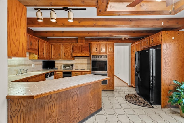 kitchen featuring tile counters, sink, kitchen peninsula, black fridge with ice dispenser, and multiple ovens