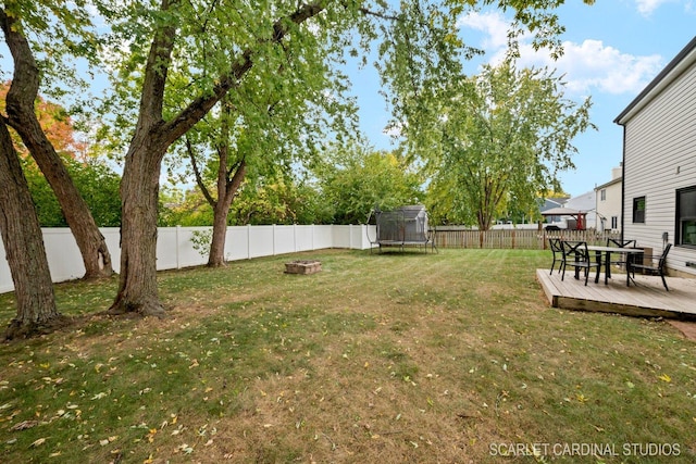 view of yard featuring a trampoline, a wooden deck, and a fire pit