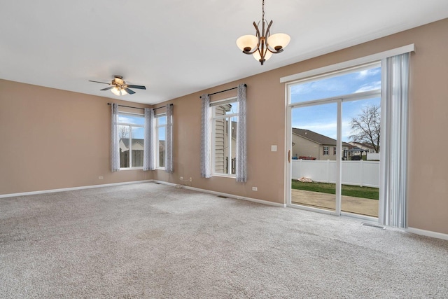 empty room with ceiling fan with notable chandelier, carpet floors, and a wealth of natural light