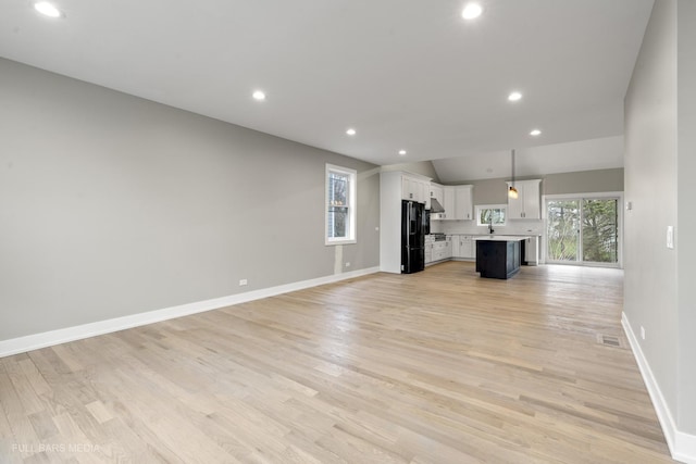 unfurnished living room with light wood-type flooring, sink, and vaulted ceiling