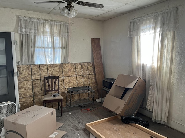 sitting room featuring ceiling fan, a drop ceiling, and wood-type flooring