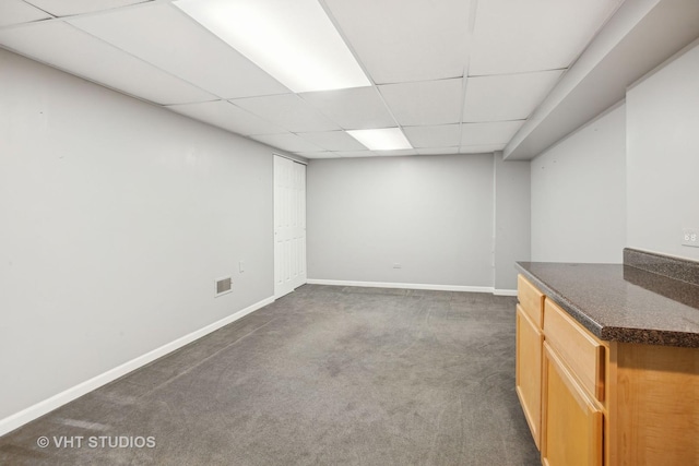 basement with a paneled ceiling and dark colored carpet