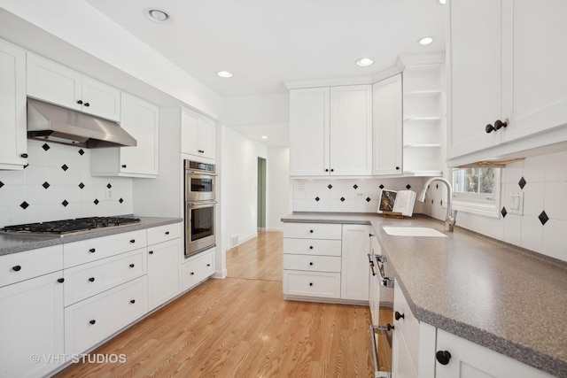 kitchen with white cabinetry, stainless steel appliances, decorative backsplash, sink, and light wood-type flooring