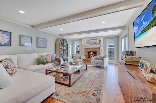 living room featuring beamed ceiling, a wealth of natural light, a fireplace, and light hardwood / wood-style flooring