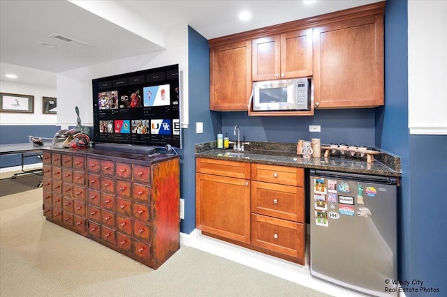 bar with sink, stainless steel refrigerator, dishwasher, light colored carpet, and dark stone counters