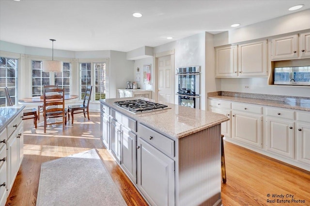 kitchen with white cabinetry, decorative light fixtures, a center island, appliances with stainless steel finishes, and light hardwood / wood-style floors