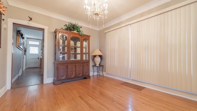 unfurnished room with crown molding, light hardwood / wood-style floors, and an inviting chandelier