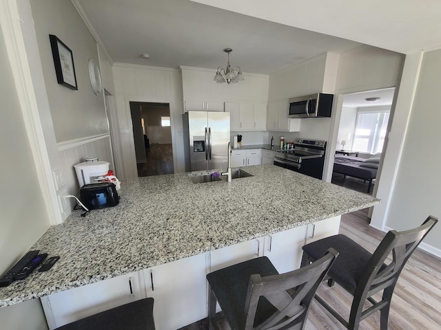 kitchen with sink, a notable chandelier, kitchen peninsula, white cabinets, and appliances with stainless steel finishes