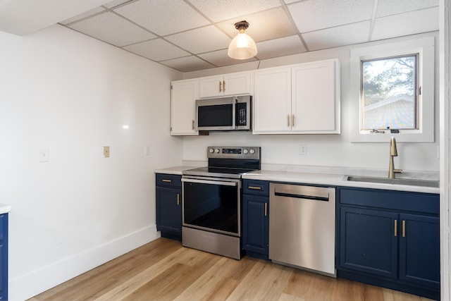 kitchen featuring appliances with stainless steel finishes, a paneled ceiling, blue cabinets, sink, and white cabinets