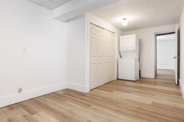 laundry area with stacked washing maching and dryer and light hardwood / wood-style flooring