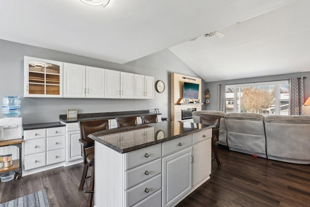 kitchen featuring vaulted ceiling, a center island, a breakfast bar, dark hardwood / wood-style floors, and white cabinetry