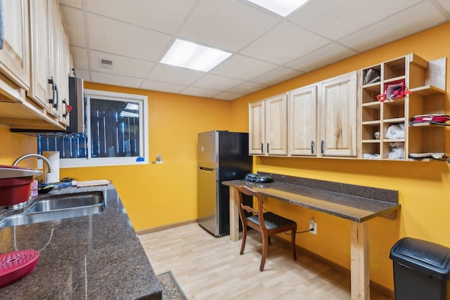 kitchen featuring sink, built in desk, a drop ceiling, light hardwood / wood-style floors, and stainless steel refrigerator