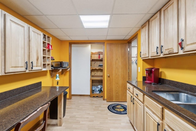 kitchen with light brown cabinetry, a drop ceiling, light wood-type flooring, and dark stone countertops