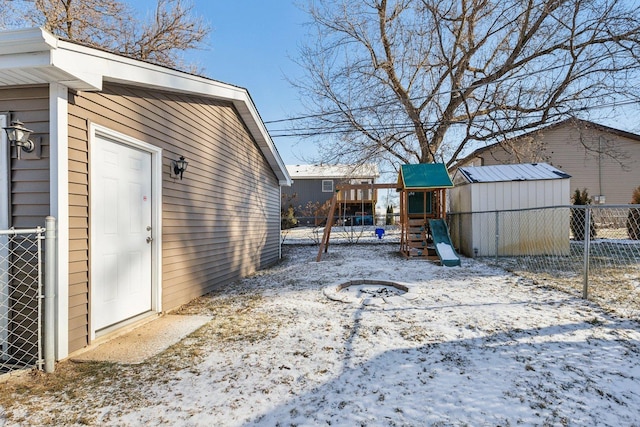 yard layered in snow with a playground and a storage unit