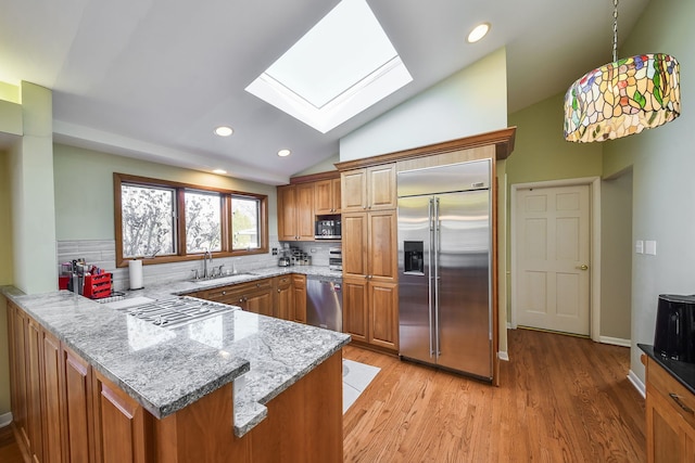 kitchen with lofted ceiling with skylight, pendant lighting, light stone counters, kitchen peninsula, and stainless steel appliances