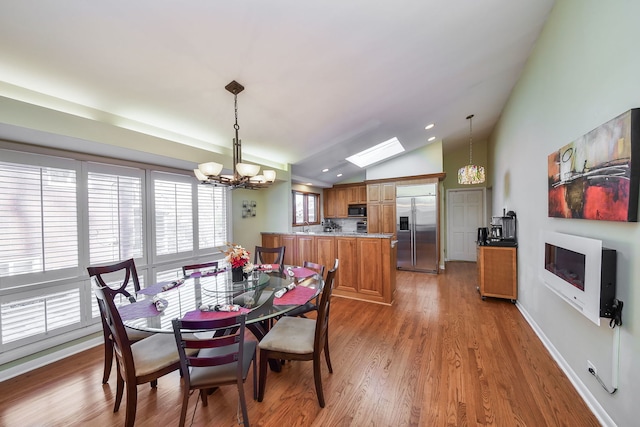 dining room featuring hardwood / wood-style flooring, lofted ceiling with skylight, and a notable chandelier