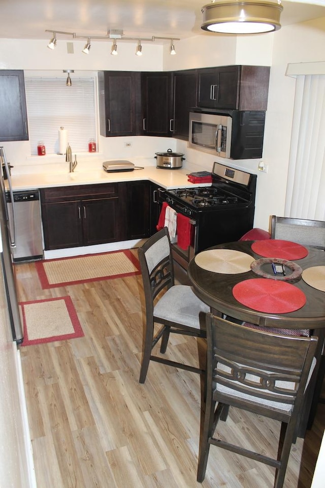 kitchen featuring dark brown cabinetry, sink, light wood-type flooring, and appliances with stainless steel finishes