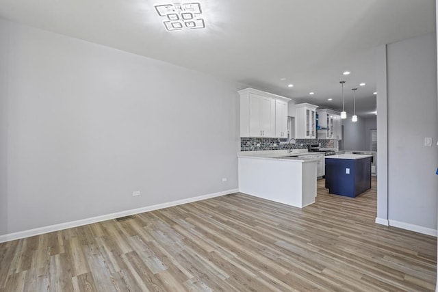 kitchen with pendant lighting, a center island, white cabinets, light hardwood / wood-style flooring, and decorative backsplash