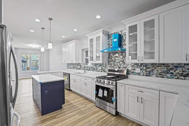 kitchen with white cabinets, appliances with stainless steel finishes, a center island, and wall chimney range hood