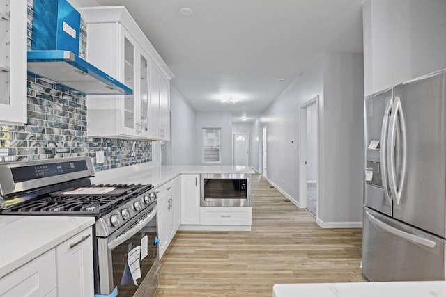 kitchen featuring light wood-type flooring, backsplash, stainless steel appliances, wall chimney range hood, and white cabinets