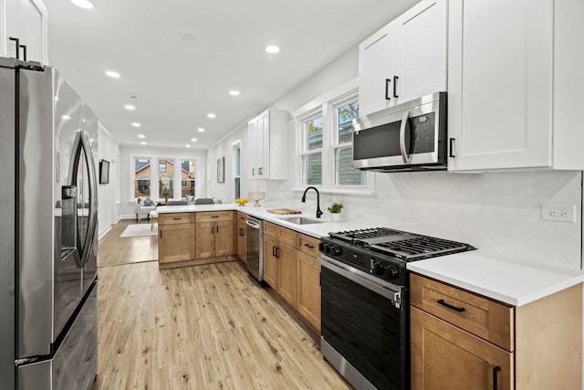 kitchen with kitchen peninsula, appliances with stainless steel finishes, tasteful backsplash, light hardwood / wood-style floors, and white cabinetry