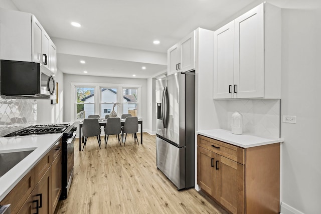 kitchen with white cabinets, appliances with stainless steel finishes, tasteful backsplash, and light hardwood / wood-style flooring