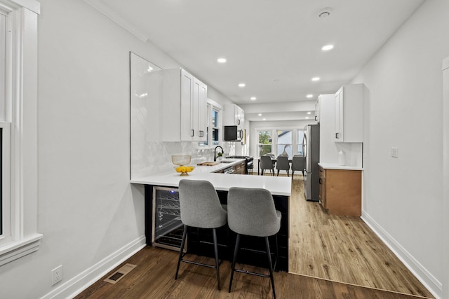 kitchen with kitchen peninsula, stainless steel fridge, white cabinetry, wood-type flooring, and a breakfast bar area