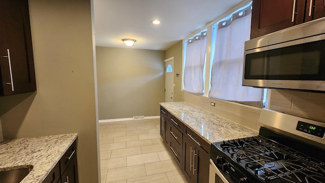 kitchen featuring light stone counters, dark brown cabinetry, appliances with stainless steel finishes, and tasteful backsplash