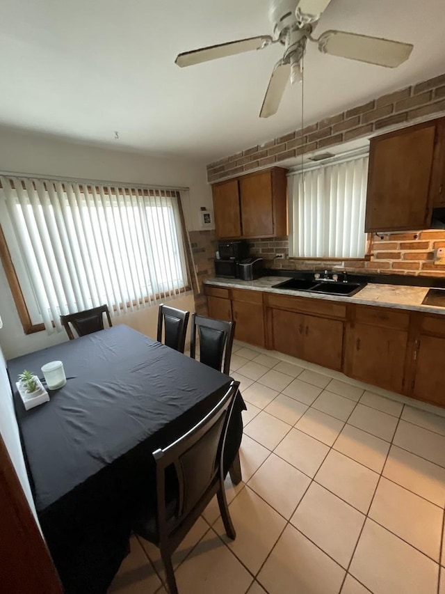 kitchen featuring ceiling fan, sink, brick wall, decorative backsplash, and light tile patterned floors