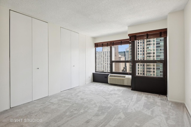 unfurnished bedroom with light colored carpet, multiple closets, a textured ceiling, and a wall mounted AC