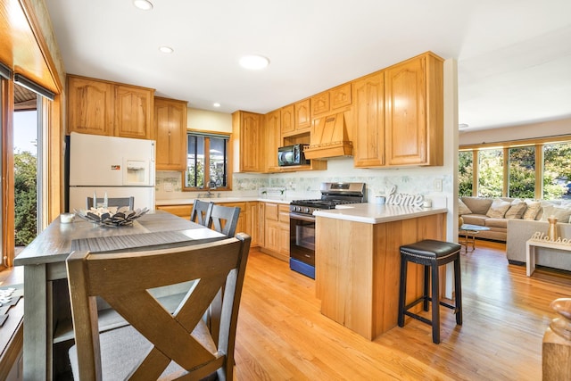 kitchen with a kitchen breakfast bar, custom range hood, gas stove, light hardwood / wood-style flooring, and white fridge with ice dispenser