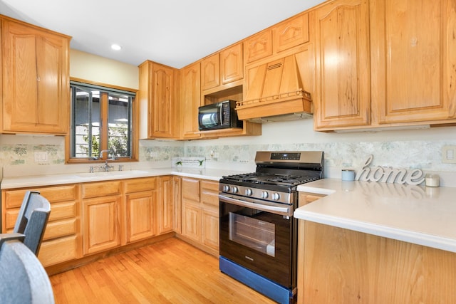 kitchen featuring gas range, sink, custom range hood, and light wood-type flooring